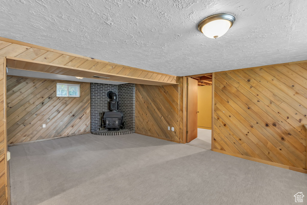 Below grade area featuring a wood stove, wooden walls, a textured ceiling, and carpet flooring