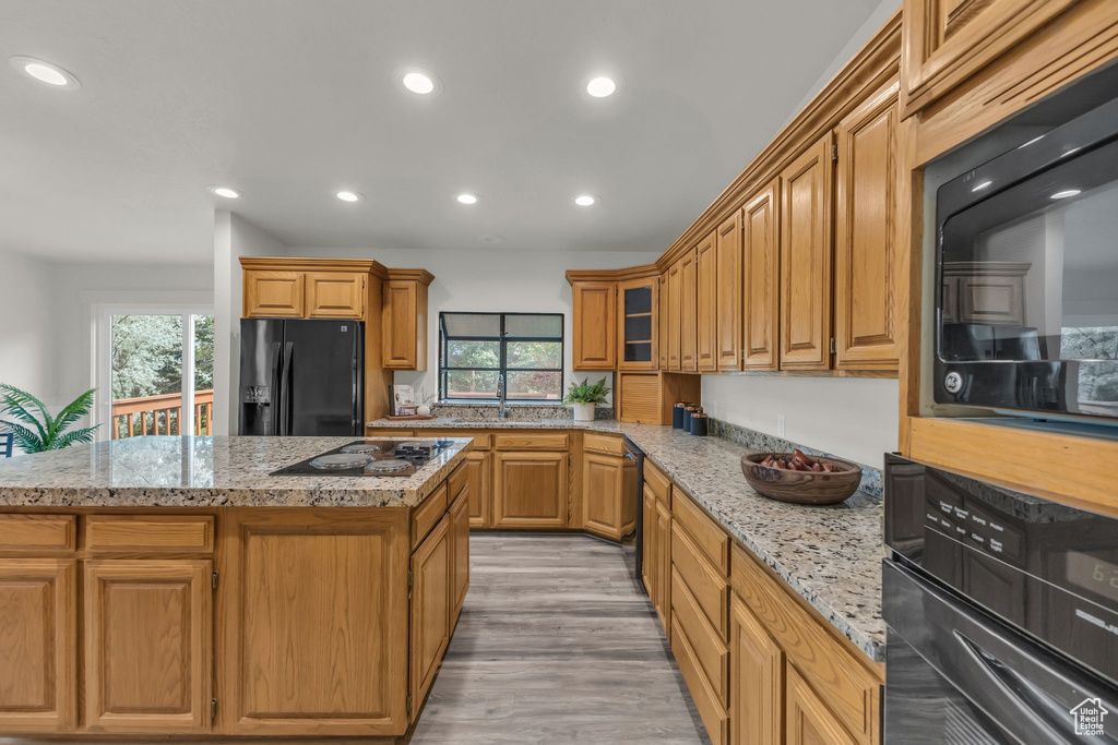 Kitchen with black appliances, plenty of natural light, light stone counters, recessed lighting, and light wood-type flooring