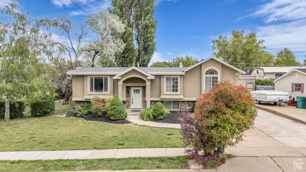 Bi-level home featuring stucco siding, stone siding, a front yard, and concrete driveway
