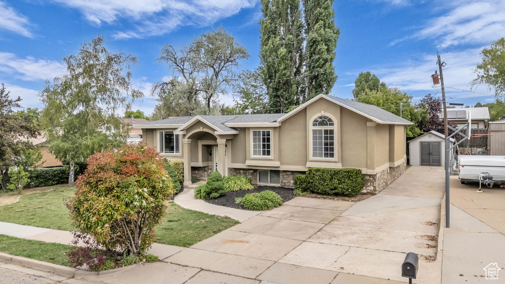View of front facade featuring a shed, stone siding, stucco siding, an outdoor structure, and concrete driveway