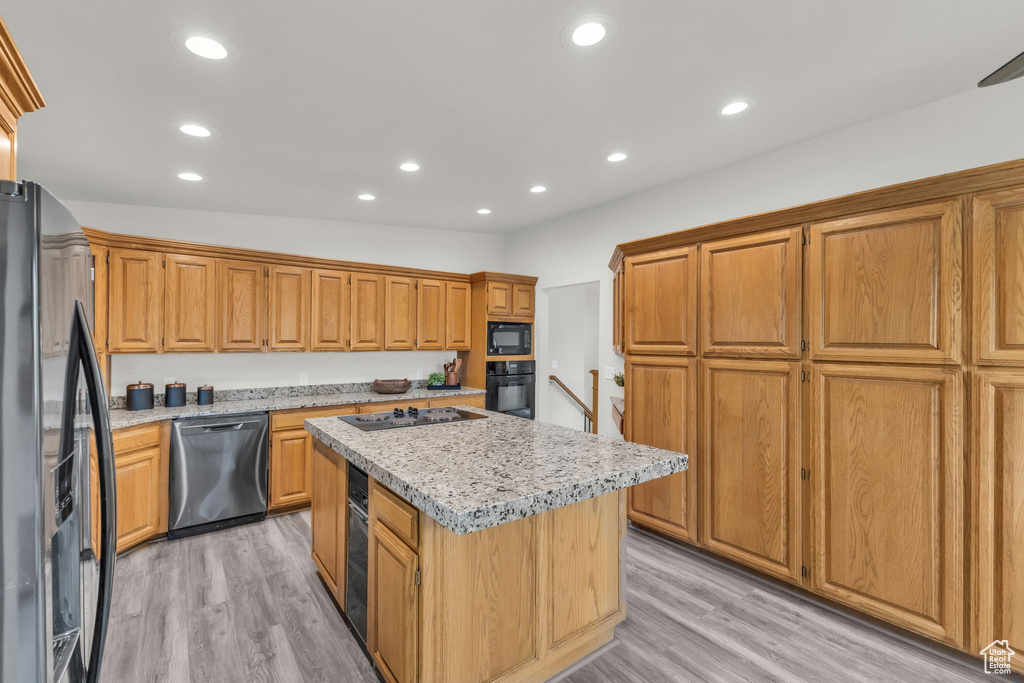 Kitchen with black appliances, a kitchen island, light wood-style flooring, recessed lighting, and light stone counters