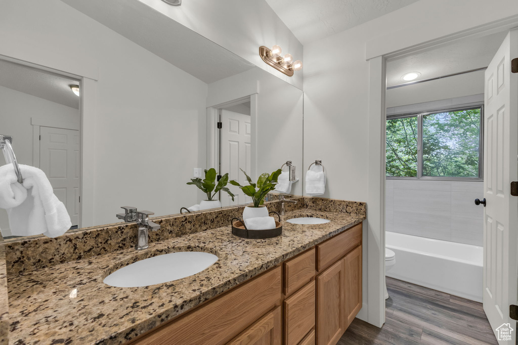 Full bathroom with wood finished floors, double vanity, toilet, and a tub