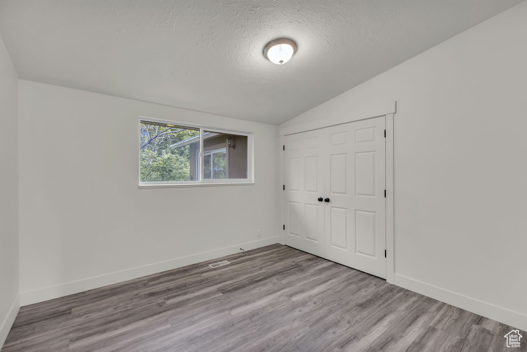 Unfurnished bedroom featuring vaulted ceiling, a textured ceiling, wood finished floors, baseboards, and a closet