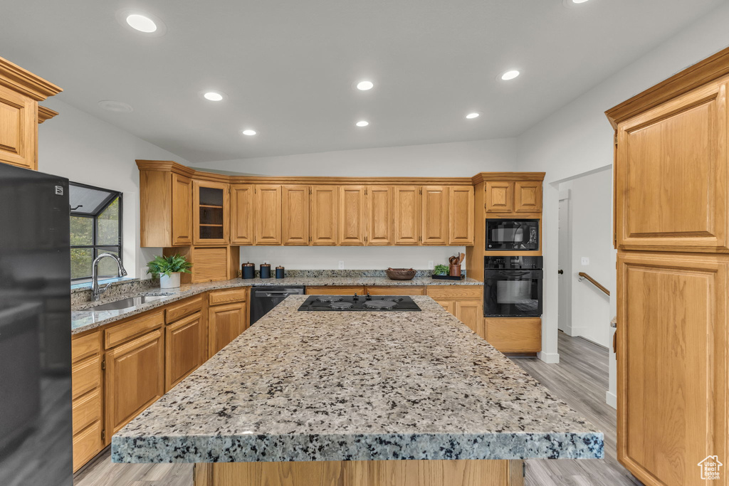 Kitchen with black appliances, lofted ceiling, a sink, a kitchen island, and light stone counters
