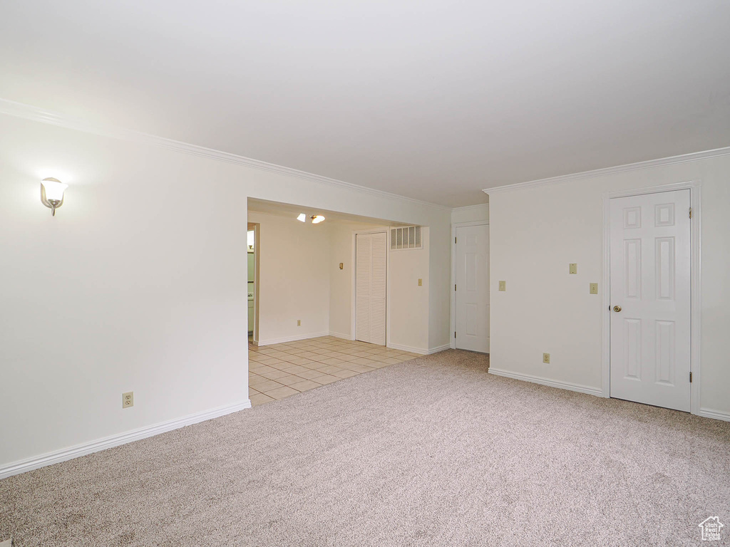 Unfurnished room featuring light carpet, ornamental molding, light tile patterned flooring, and baseboards