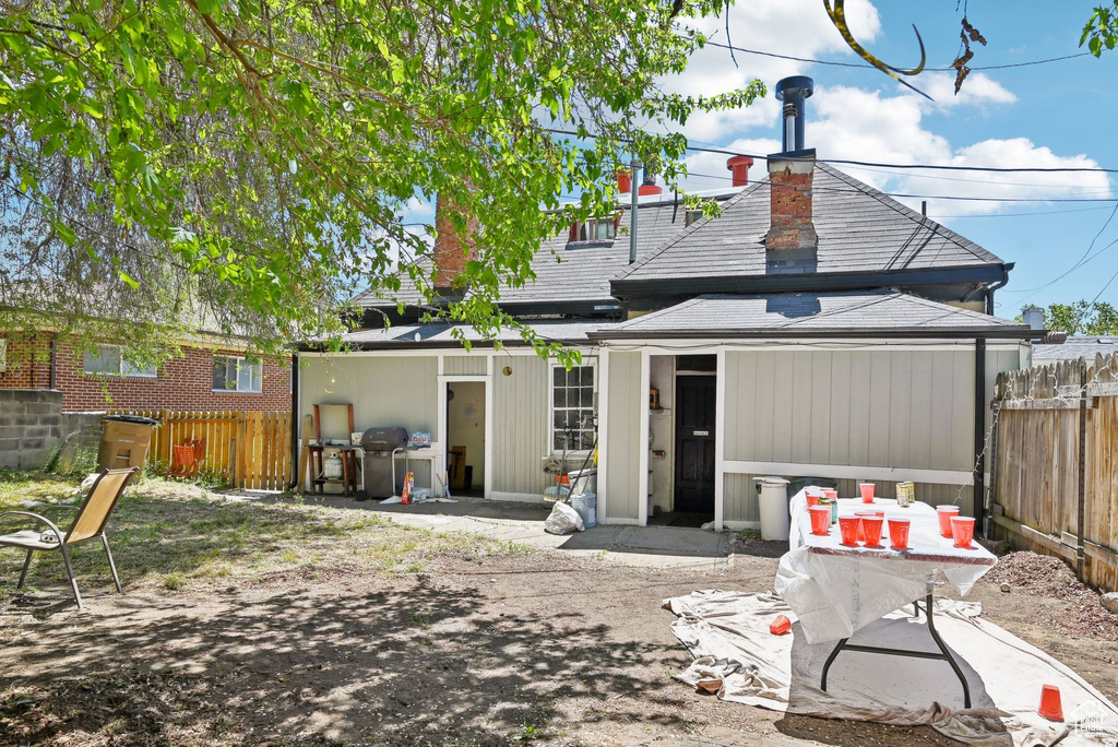 Rear view of house featuring fence, roof with shingles, and a chimney