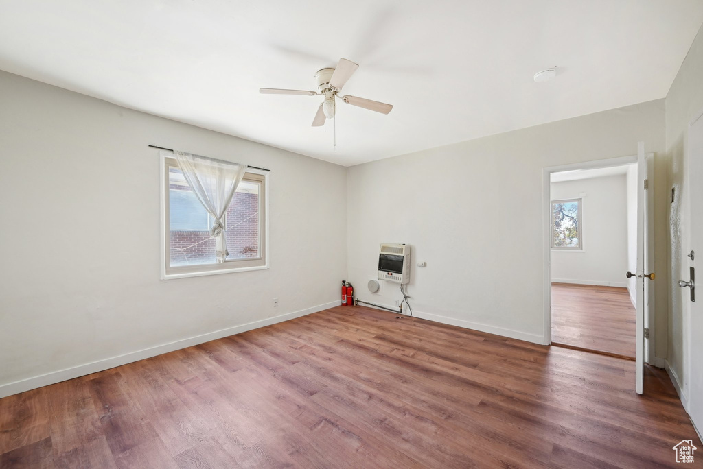 Empty room with heating unit, a ceiling fan, wood finished floors, and baseboards