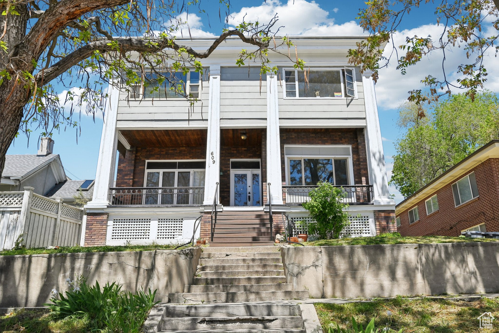 View of front of home with brick siding, a porch, stairs, and fence