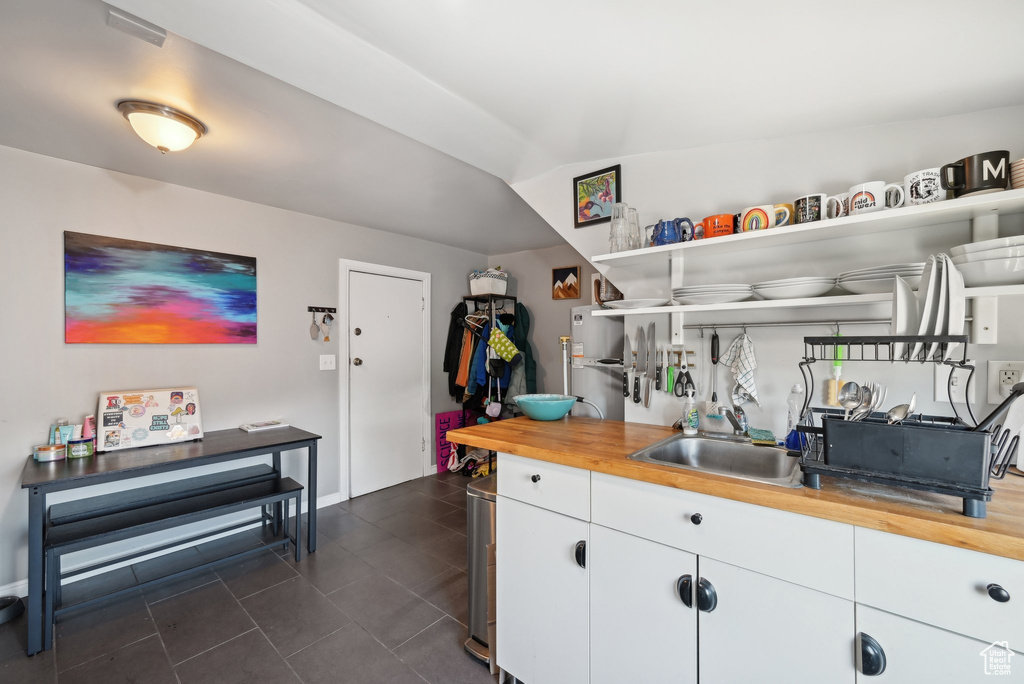Kitchen featuring a sink, open shelves, wooden counters, white cabinets, and dark tile patterned flooring