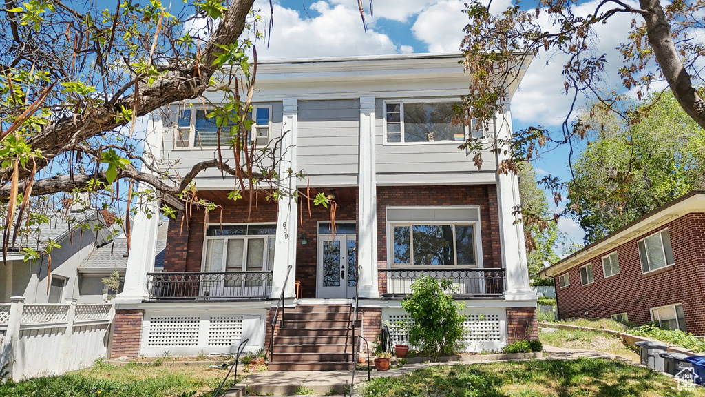 View of front facade featuring a porch, brick siding, stairway, and fence