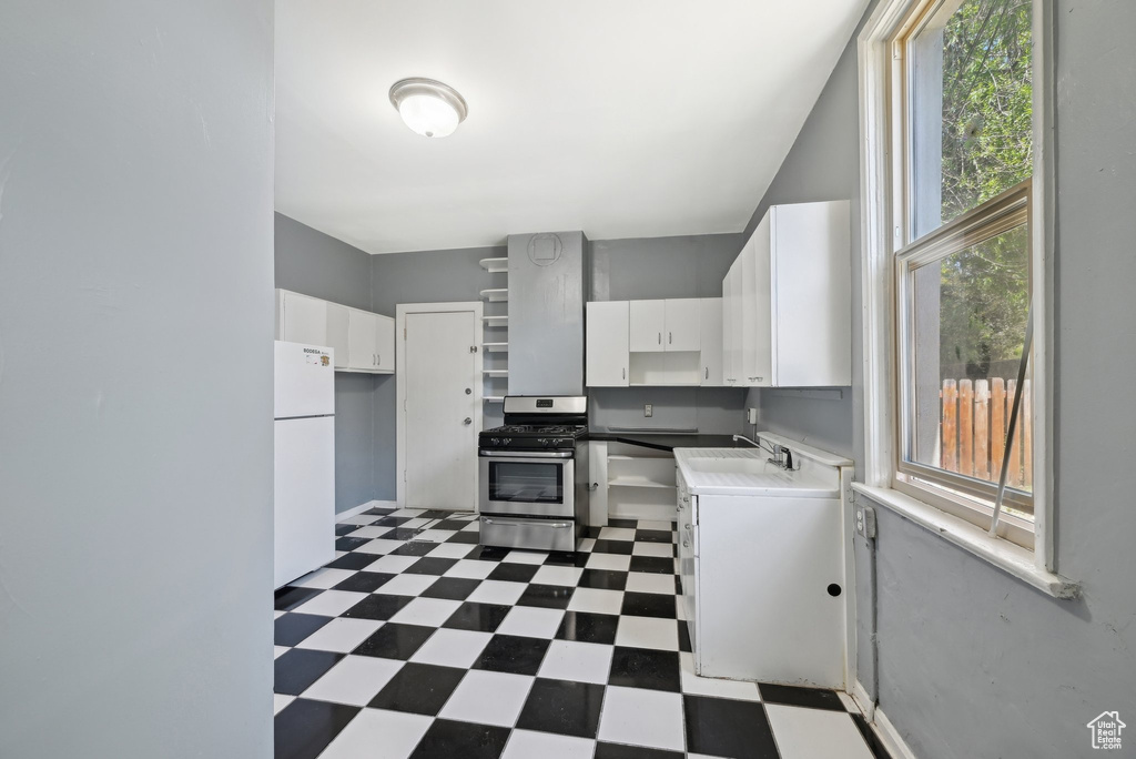 Kitchen with stainless steel range with gas stovetop, dark floors, freestanding refrigerator, and healthy amount of natural light