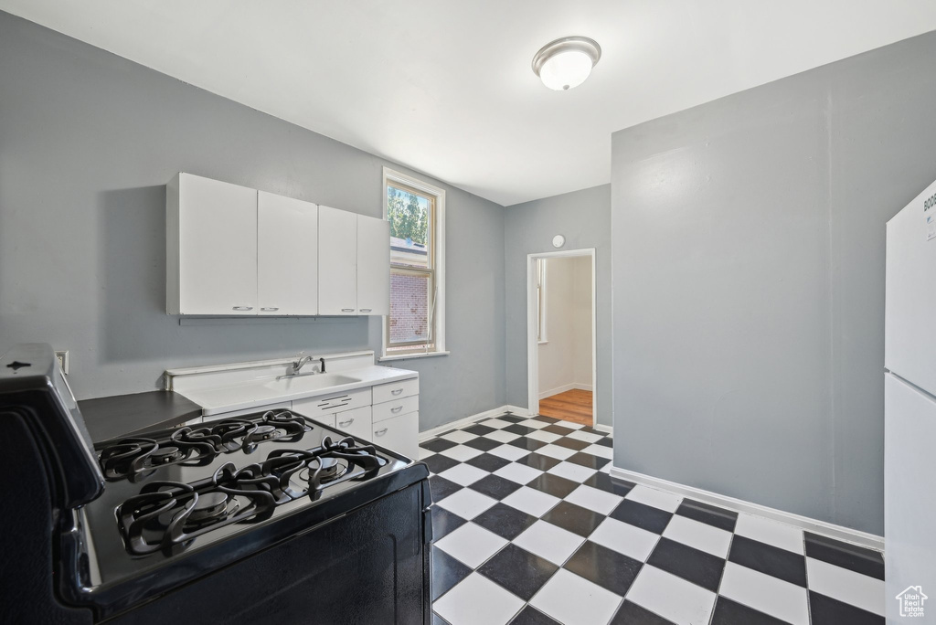 Kitchen with black range with gas stovetop, light flooring, a sink, white cabinets, and light countertops