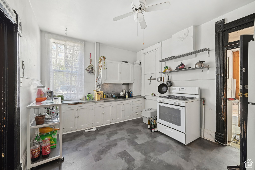 Kitchen featuring white gas range, open shelves, a ceiling fan, white cabinets, and a sink