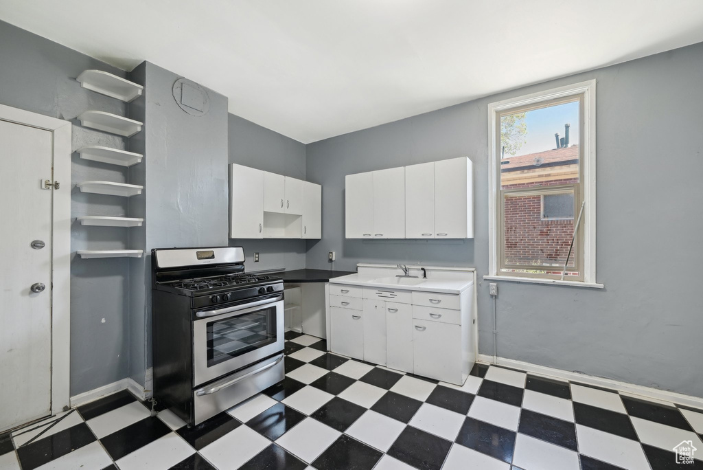 Kitchen with stainless steel gas range, dark flooring, white cabinets, a sink, and baseboards