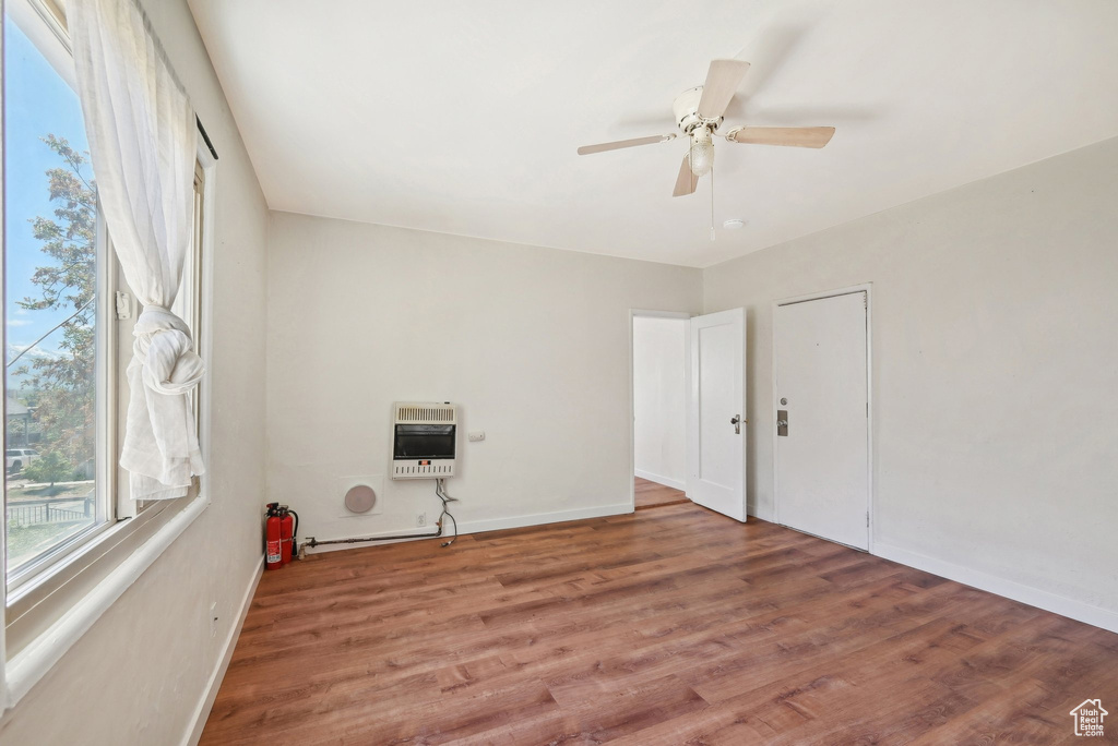 Spare room with heating unit, wood finished floors, a ceiling fan, and baseboards