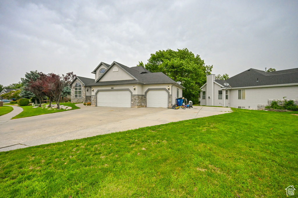 View of front of property featuring an attached garage, concrete driveway, a front lawn, stone siding, and stucco siding