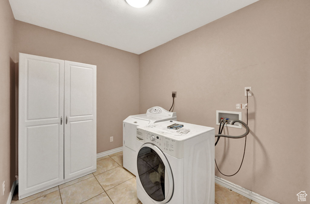 Clothes washing area with washer / clothes dryer, cabinet space, baseboards, and light tile patterned floors