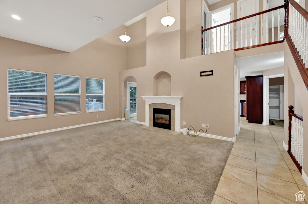 Unfurnished living room featuring baseboards, a high ceiling, tile patterned flooring, a tile fireplace, and carpet floors