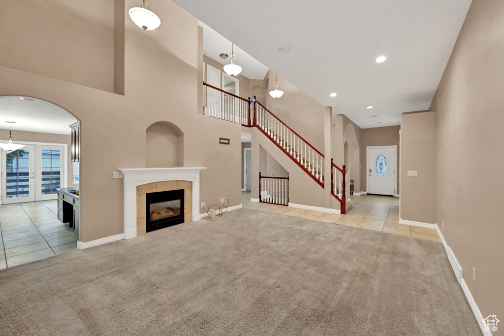 Unfurnished living room featuring carpet floors, tile patterned flooring, baseboards, a towering ceiling, and recessed lighting