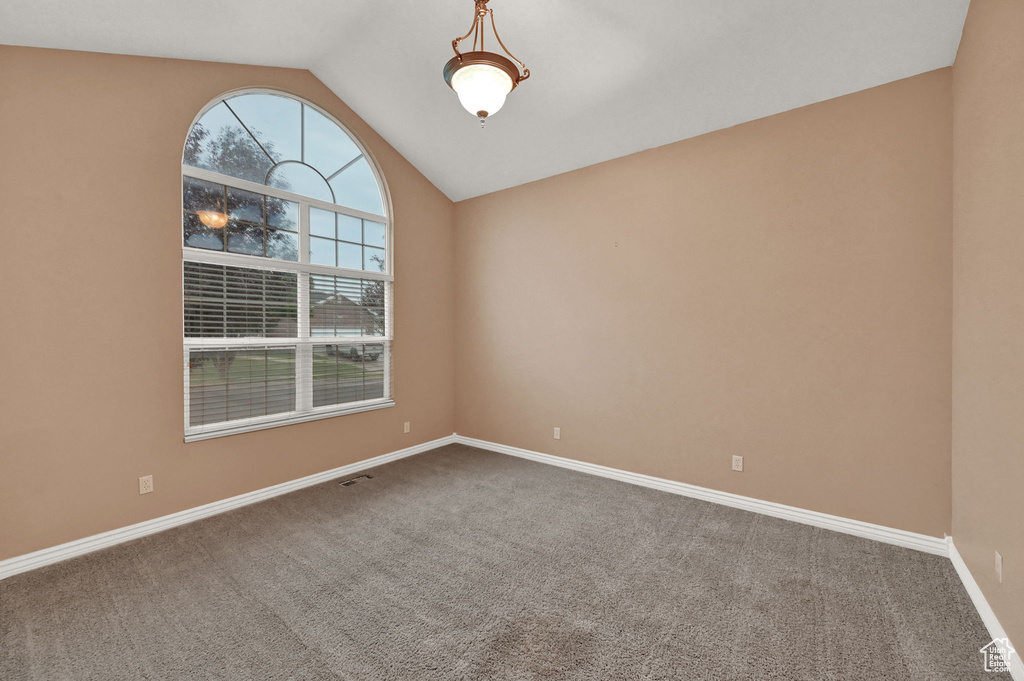 Carpeted spare room featuring vaulted ceiling and baseboards