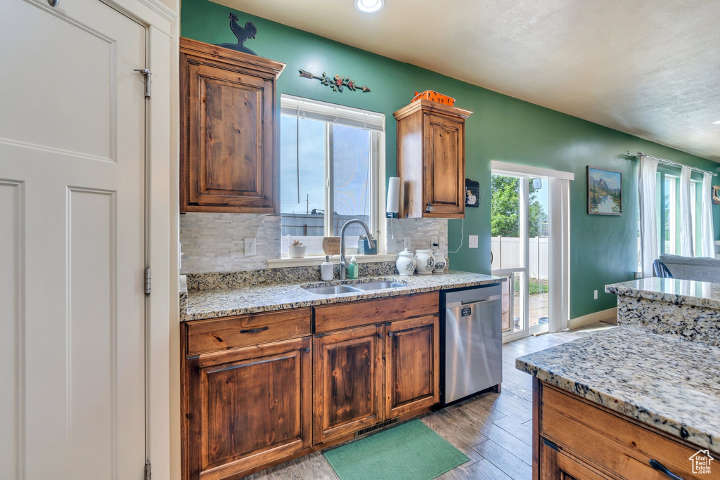 Kitchen with stainless steel dishwasher, a sink, tasteful backsplash, light wood-style floors, and brown cabinetry