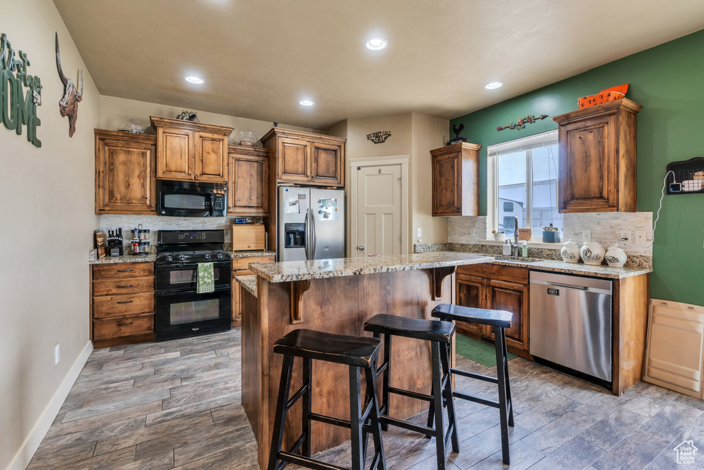 Kitchen featuring black appliances, backsplash, a sink, wood finished floors, and recessed lighting
