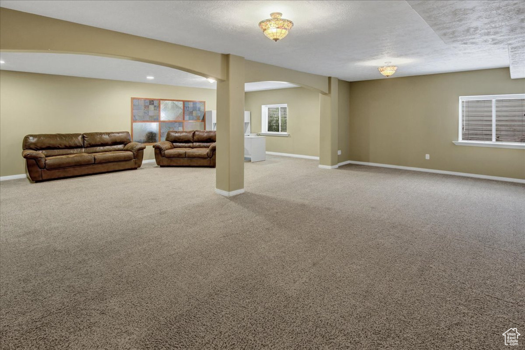 Unfurnished living room featuring arched walkways, carpet floors, and baseboards
