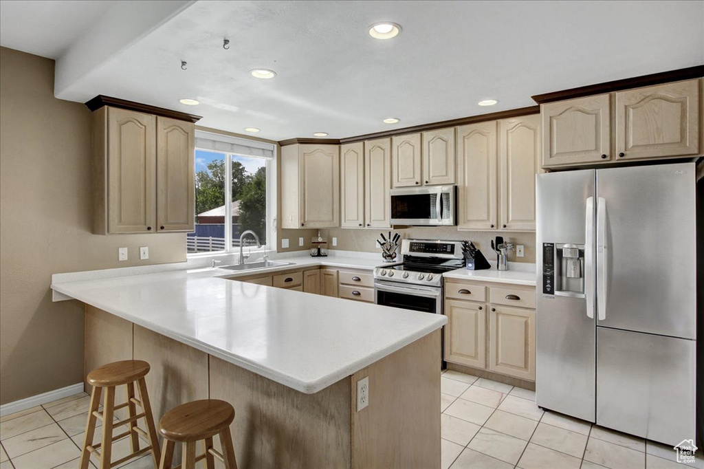 Kitchen with appliances with stainless steel finishes, a sink, a breakfast bar, recessed lighting, and light countertops