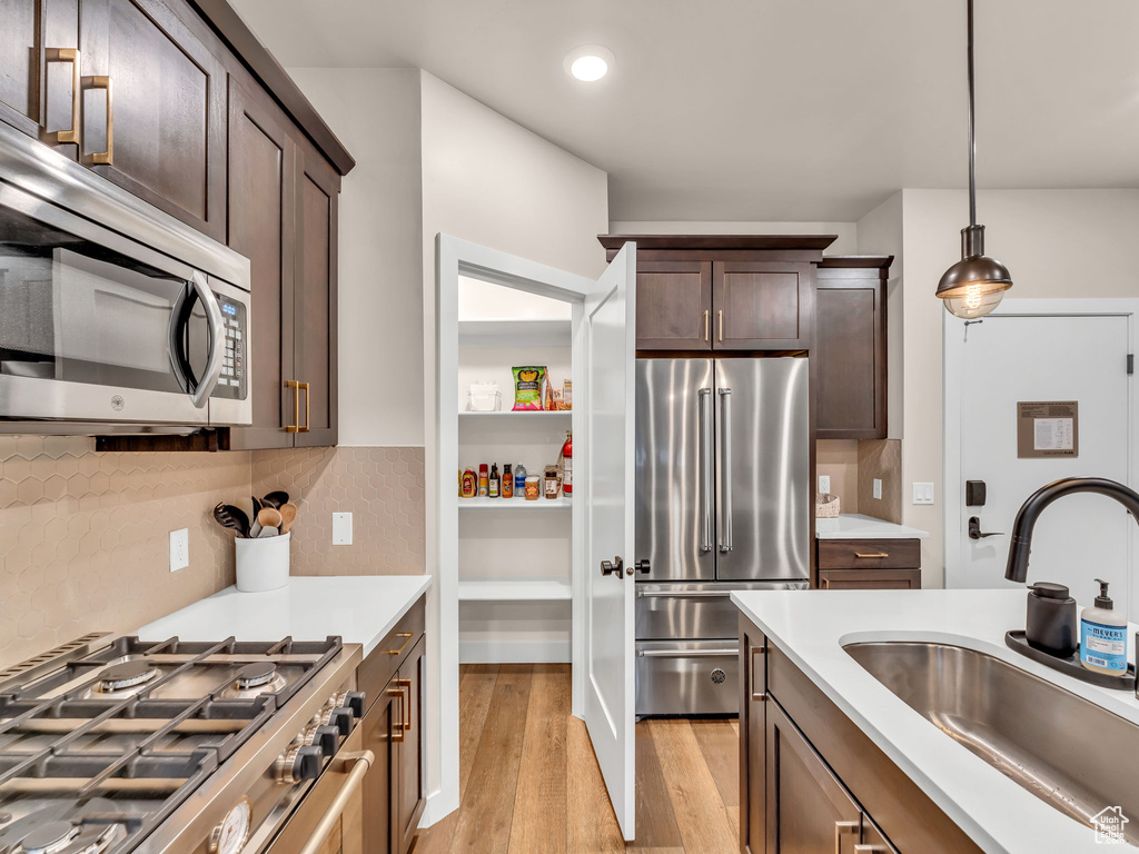 Kitchen featuring appliances with stainless steel finishes, a sink, light wood-style flooring, light countertops, and decorative light fixtures