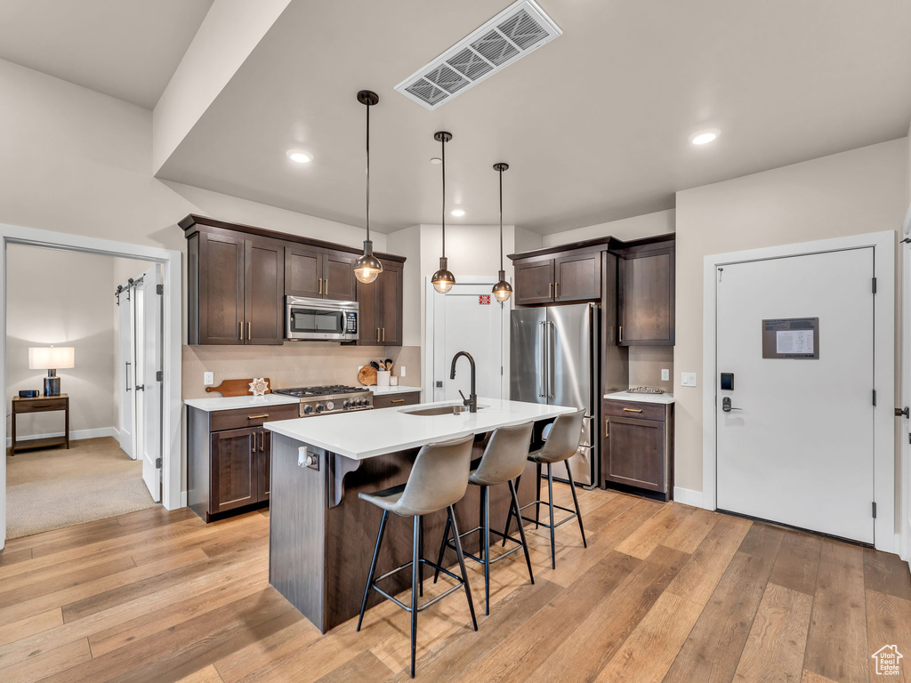 Kitchen with appliances with stainless steel finishes, a sink, a kitchen breakfast bar, dark brown cabinets, and light countertops