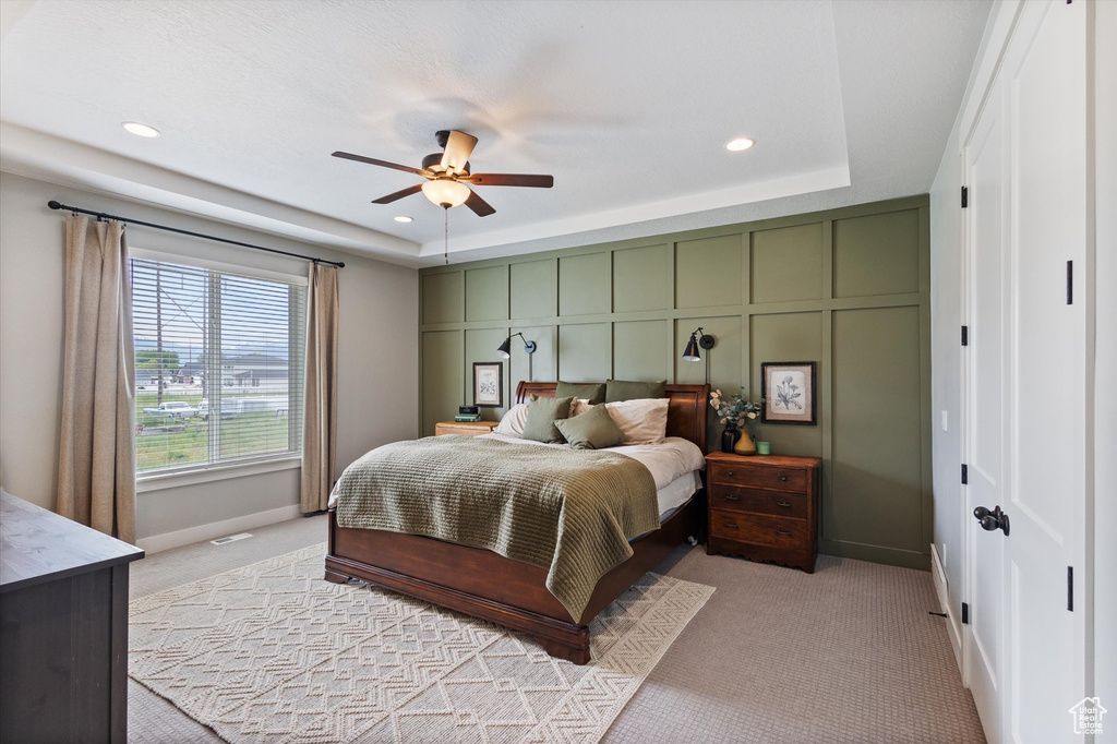Bedroom with light carpet, a raised ceiling, baseboards, recessed lighting, and a ceiling fan