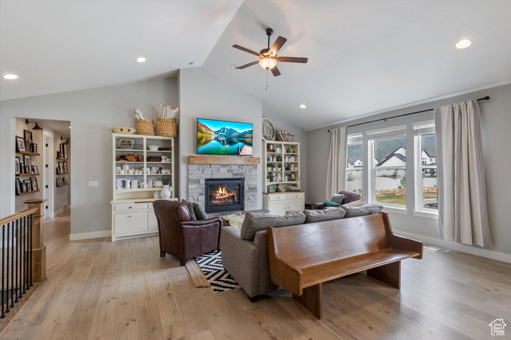 Living area with vaulted ceiling, ceiling fan, a stone fireplace, light wood finished floors, and baseboards