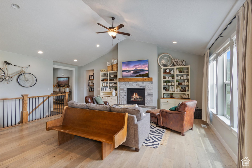 Living area featuring light wood finished floors, lofted ceiling, a stone fireplace, ceiling fan, and recessed lighting