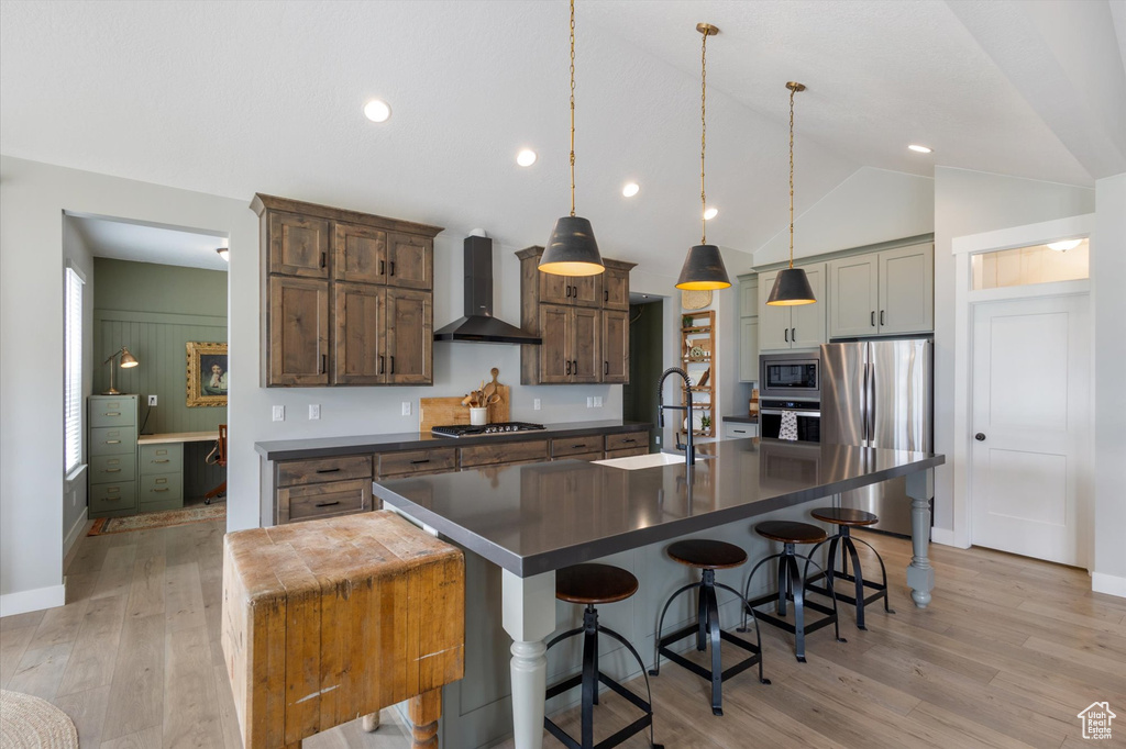 Kitchen with wall chimney exhaust hood, stainless steel appliances, dark countertops, a sink, and lofted ceiling