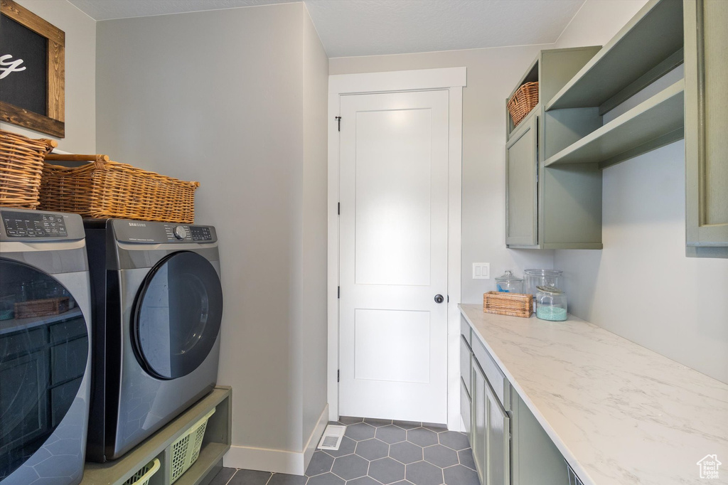 Laundry area featuring separate washer and dryer, dark tile patterned floors, cabinet space, and baseboards