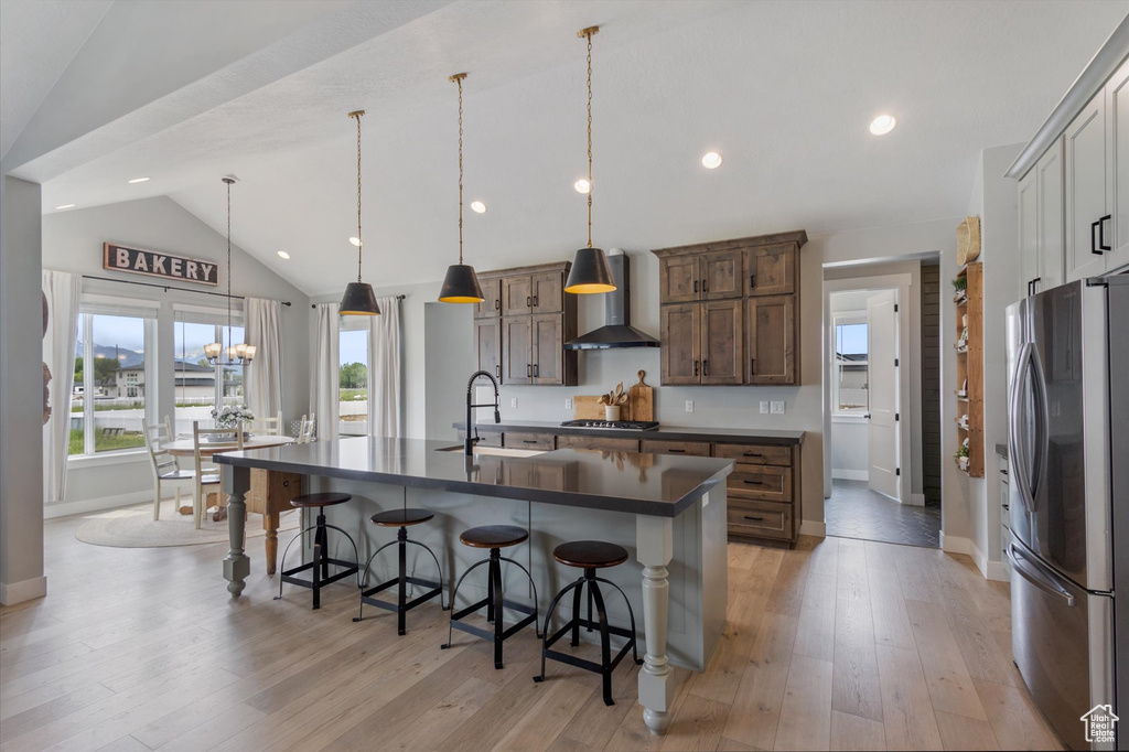 Kitchen with stainless steel appliances, wall chimney range hood, a sink, dark countertops, and baseboards