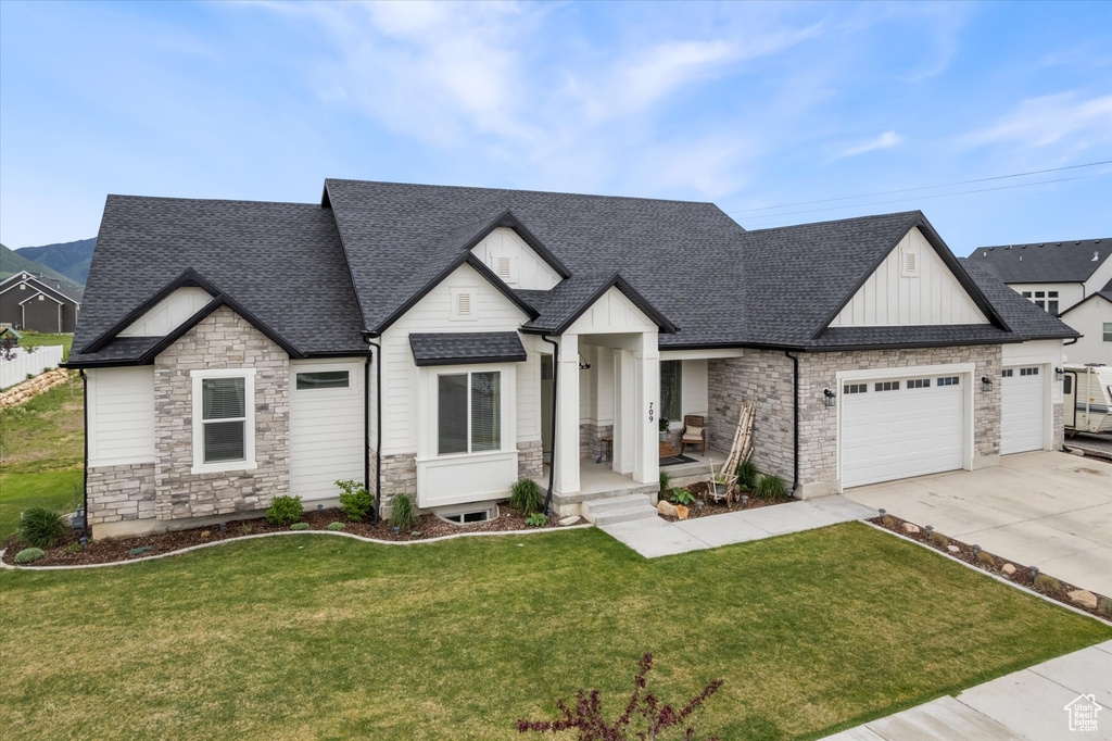 Modern farmhouse style home featuring stone siding, a garage, concrete driveway, a shingled roof, and board and batten siding