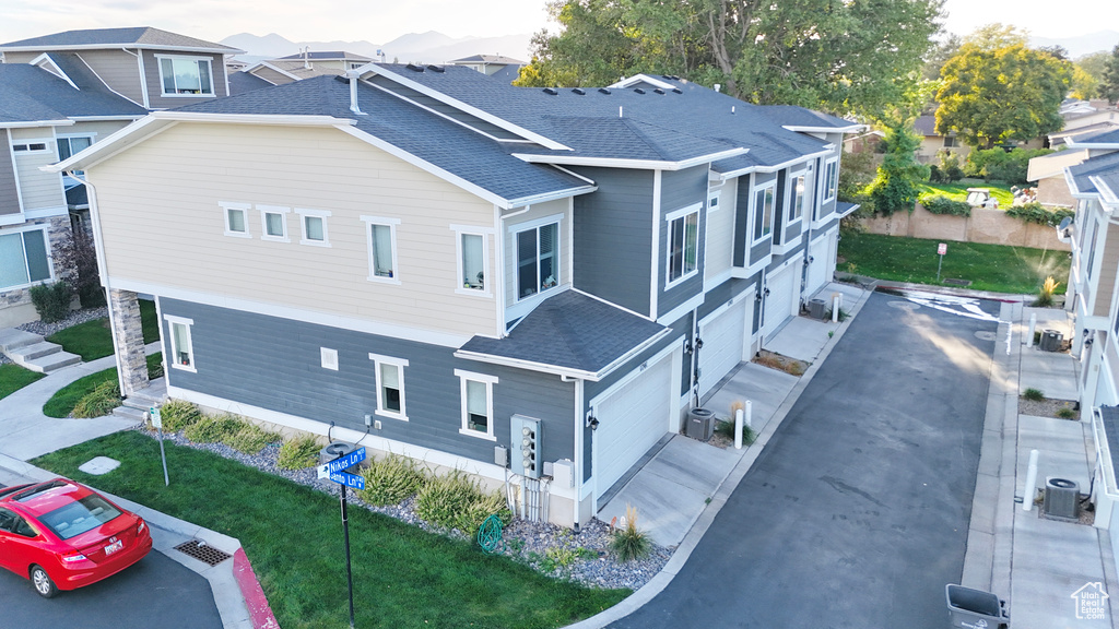 View of property exterior featuring roof with shingles, an attached garage, central AC unit, and a lawn