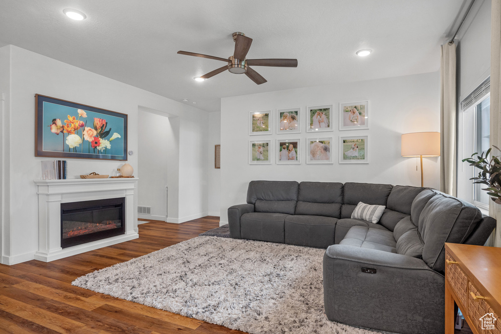 Living room featuring a ceiling fan, dark wood finished floors, a glass covered fireplace, baseboards, and recessed lighting