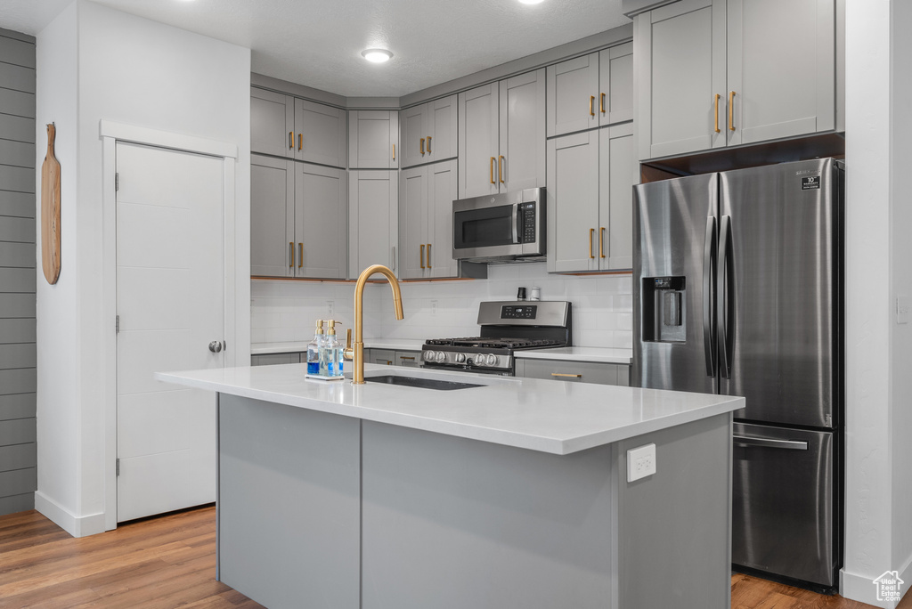 Kitchen with stainless steel appliances, a sink, gray cabinetry, light wood-type flooring, and light countertops