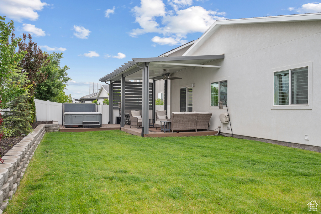 Back of property featuring a hot tub, outdoor lounge area, a ceiling fan, and stucco siding