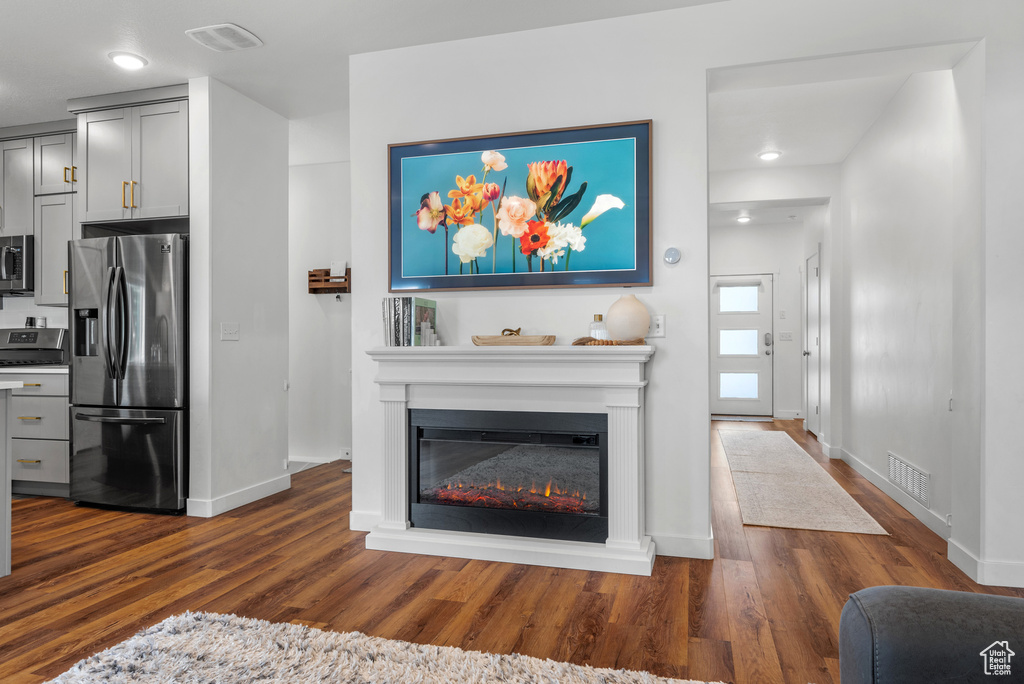 Living room featuring dark wood-type flooring, baseboards, a glass covered fireplace, and recessed lighting