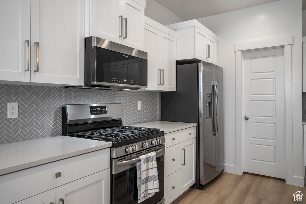 Kitchen with stainless steel appliances, decorative backsplash, light countertops, light wood-style floors, and white cabinetry