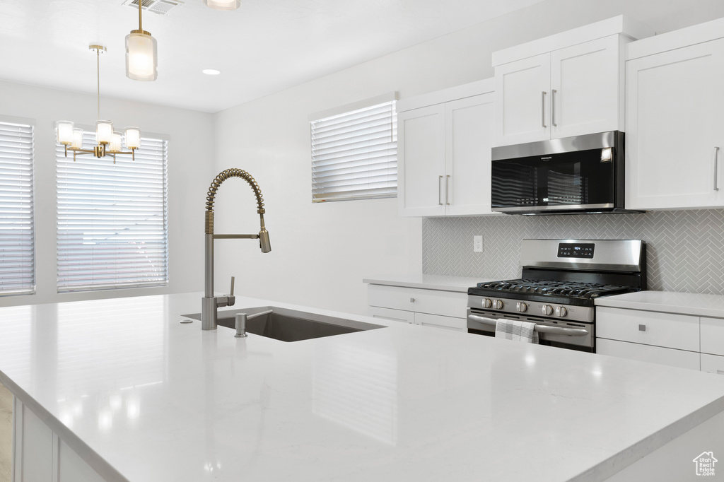 Kitchen featuring stainless steel appliances, a sink, tasteful backsplash, a chandelier, and pendant lighting