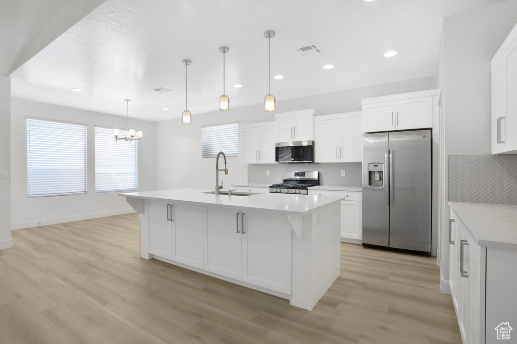 Kitchen featuring stainless steel appliances, a sink, a chandelier, light countertops, and backsplash