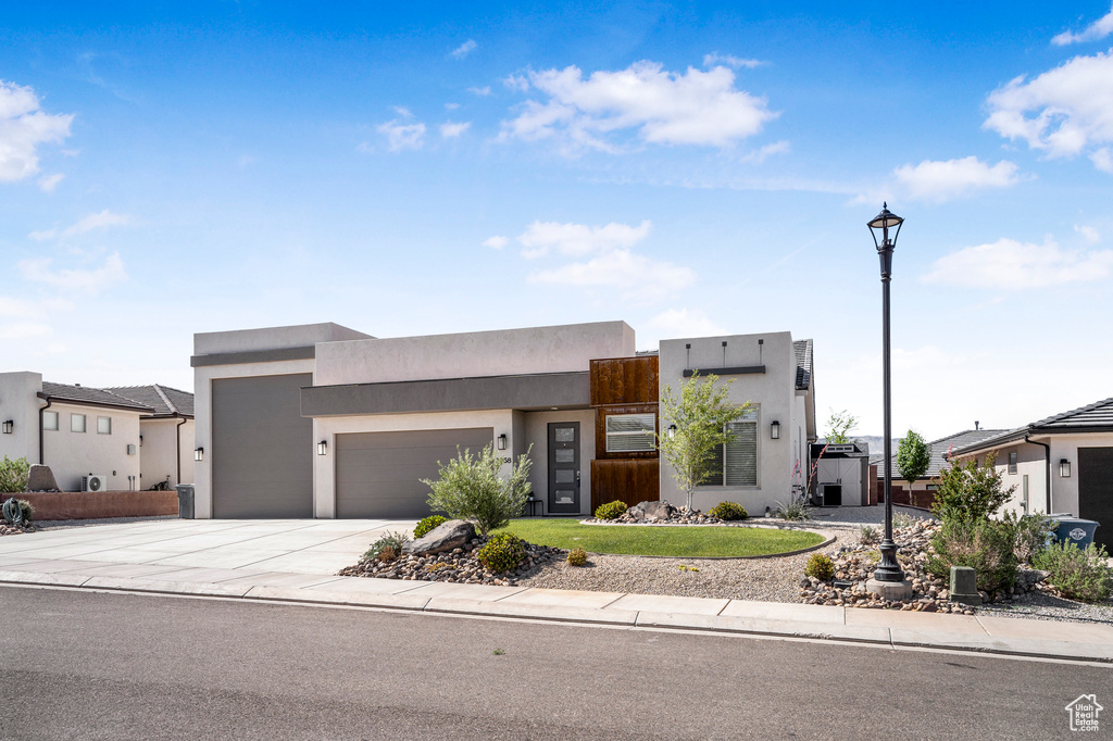 Contemporary house with an attached garage, driveway, stucco siding, and a front lawn