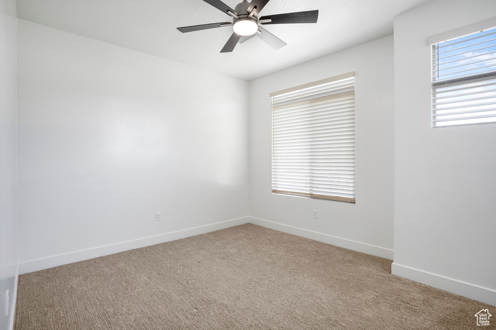 Unfurnished room featuring light colored carpet, healthy amount of natural light, a ceiling fan, and baseboards