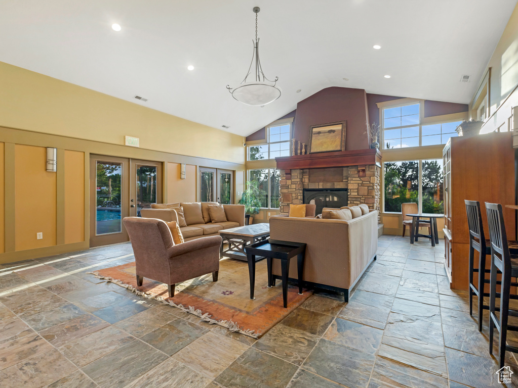 Living room with stone tile flooring, high vaulted ceiling, a stone fireplace, recessed lighting, and french doors