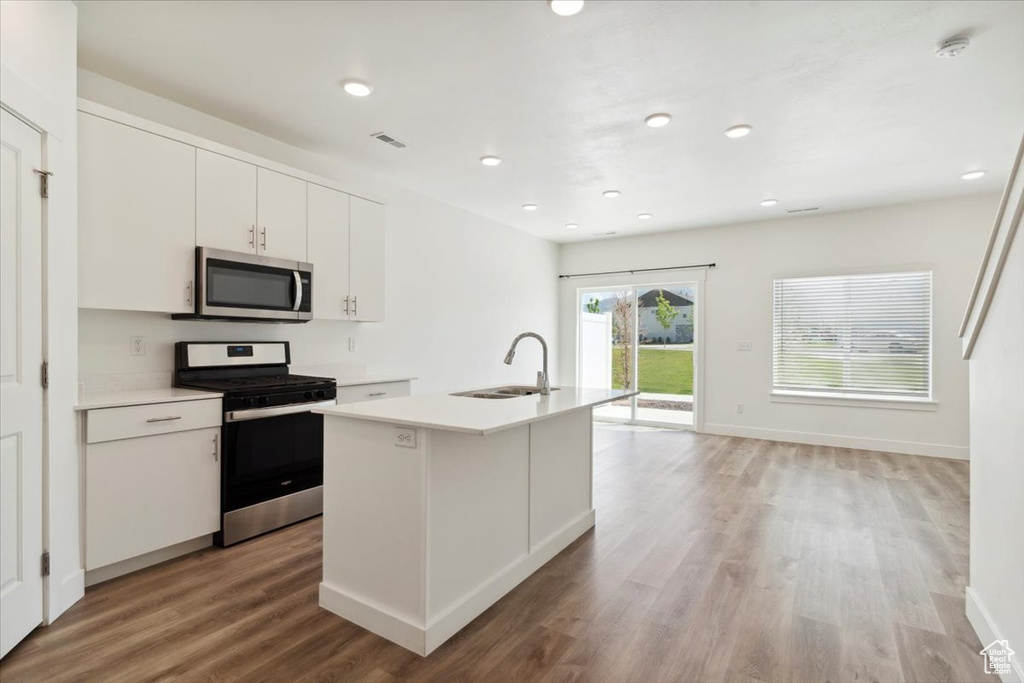Kitchen featuring appliances with stainless steel finishes, a sink, light wood-style flooring, light countertops, and white cabinets