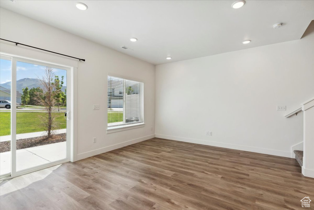 Unfurnished living room featuring healthy amount of natural light, stairs, wood finished floors, baseboards, and recessed lighting
